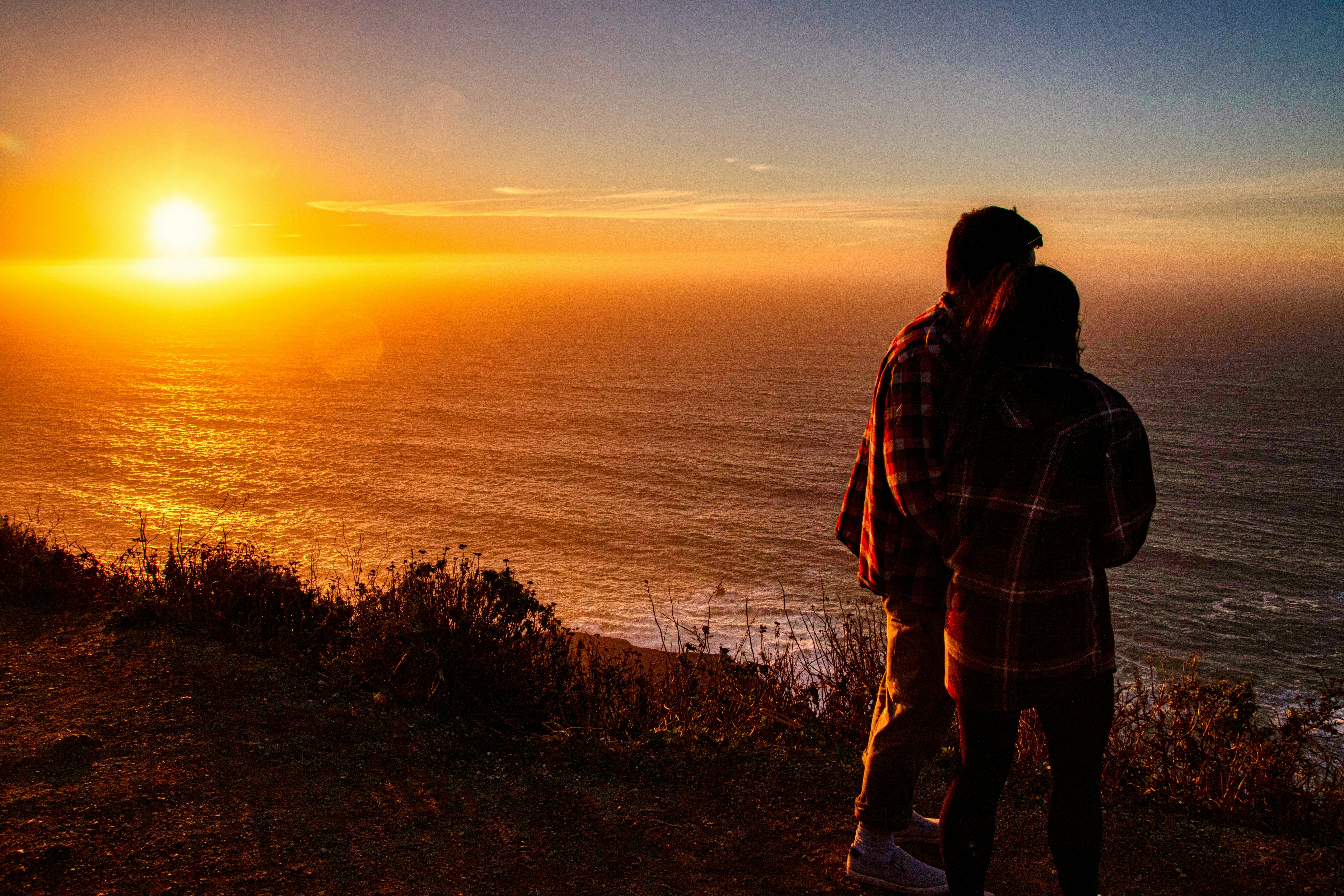 man and woman standing on island facing the ocean during golden hour